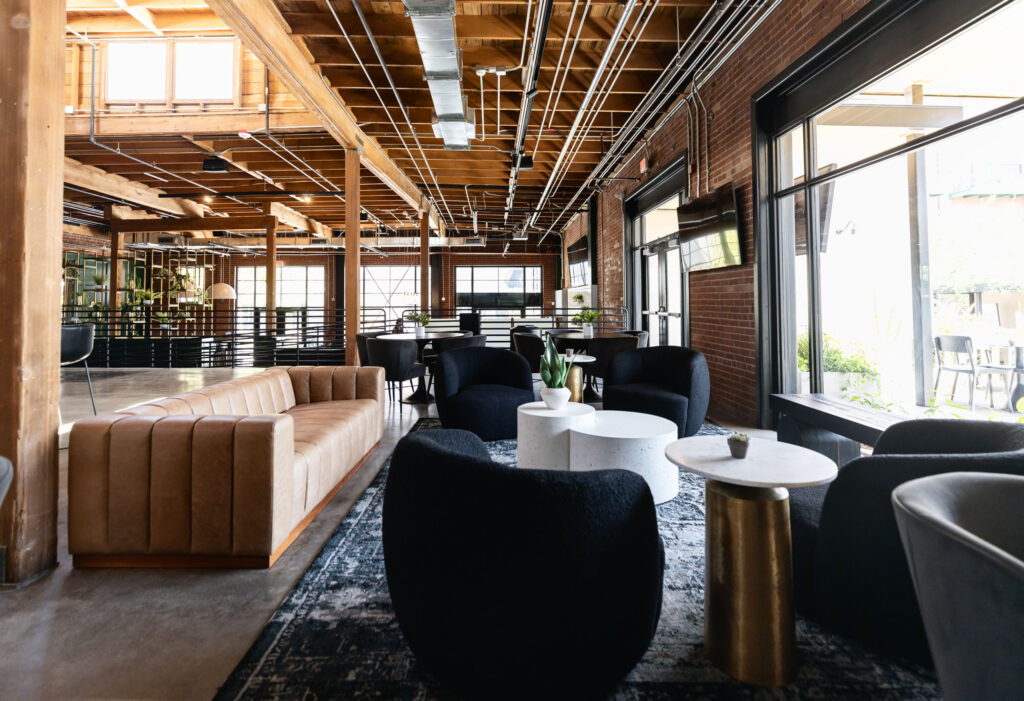 Image 1: Industrial lounge with exposed ceiling, brick walls, caramel channel-tufted sofa, black accent chairs, and marble coffee tables.