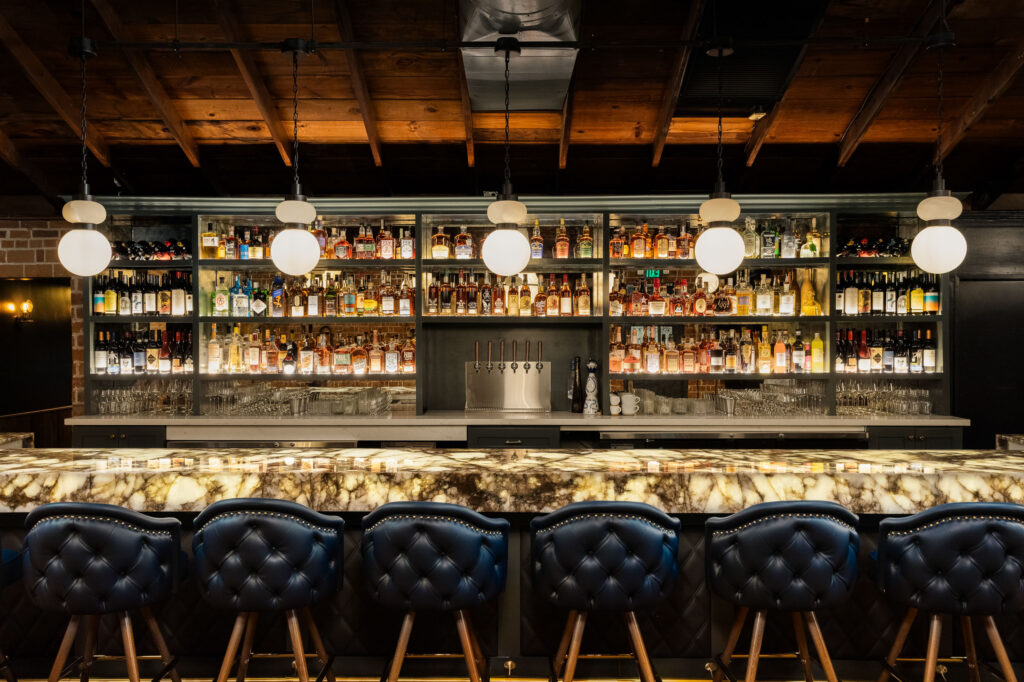Bar area with wooden beam ceiling, globe pendant lights, and illuminated shelves of spirits.