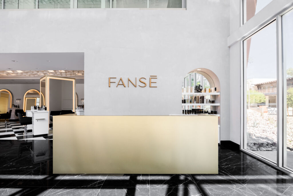 Modern FANSÉ salon reception featuring a sleek gold desk, minimalist white walls, and black marble flooring.