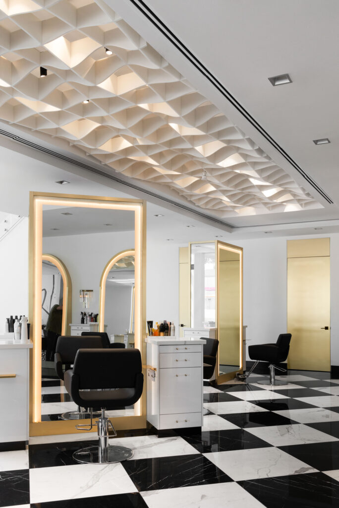Elegant styling area with textured ceiling, illuminated gold-framed mirrors, and contemporary black chairs.