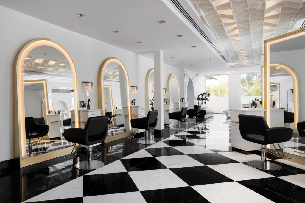 Luxurious salon with gold-framed arched mirrors, black styling chairs, and striking black and white checkered floor.